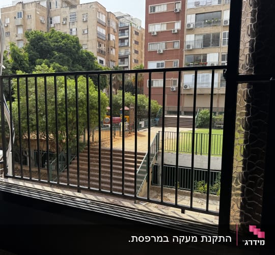 נוף מבעד לחלון עם סורגים, בניינים ועצים ברקע
